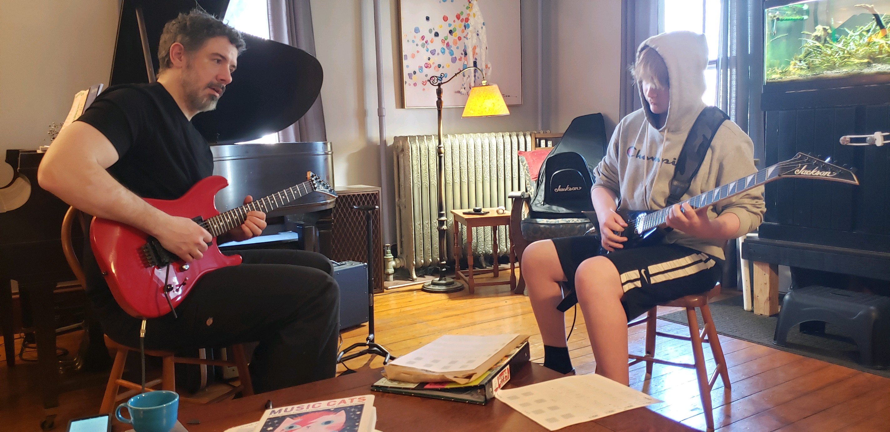 Jamie Barry teaching a student guitar in his studio, both seated and playing electric guitars